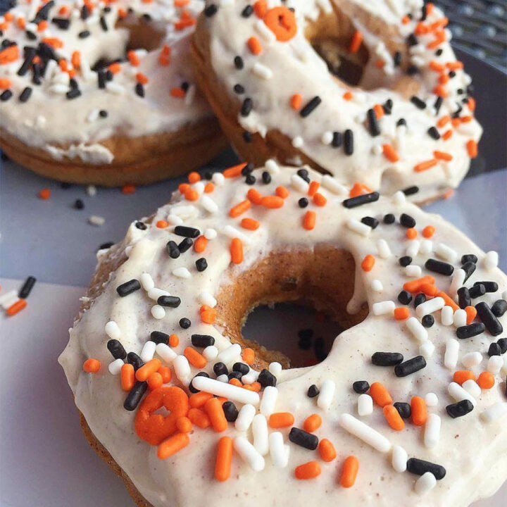 three donuts covered with white frosting and topped with black, white, and orange sprinkles