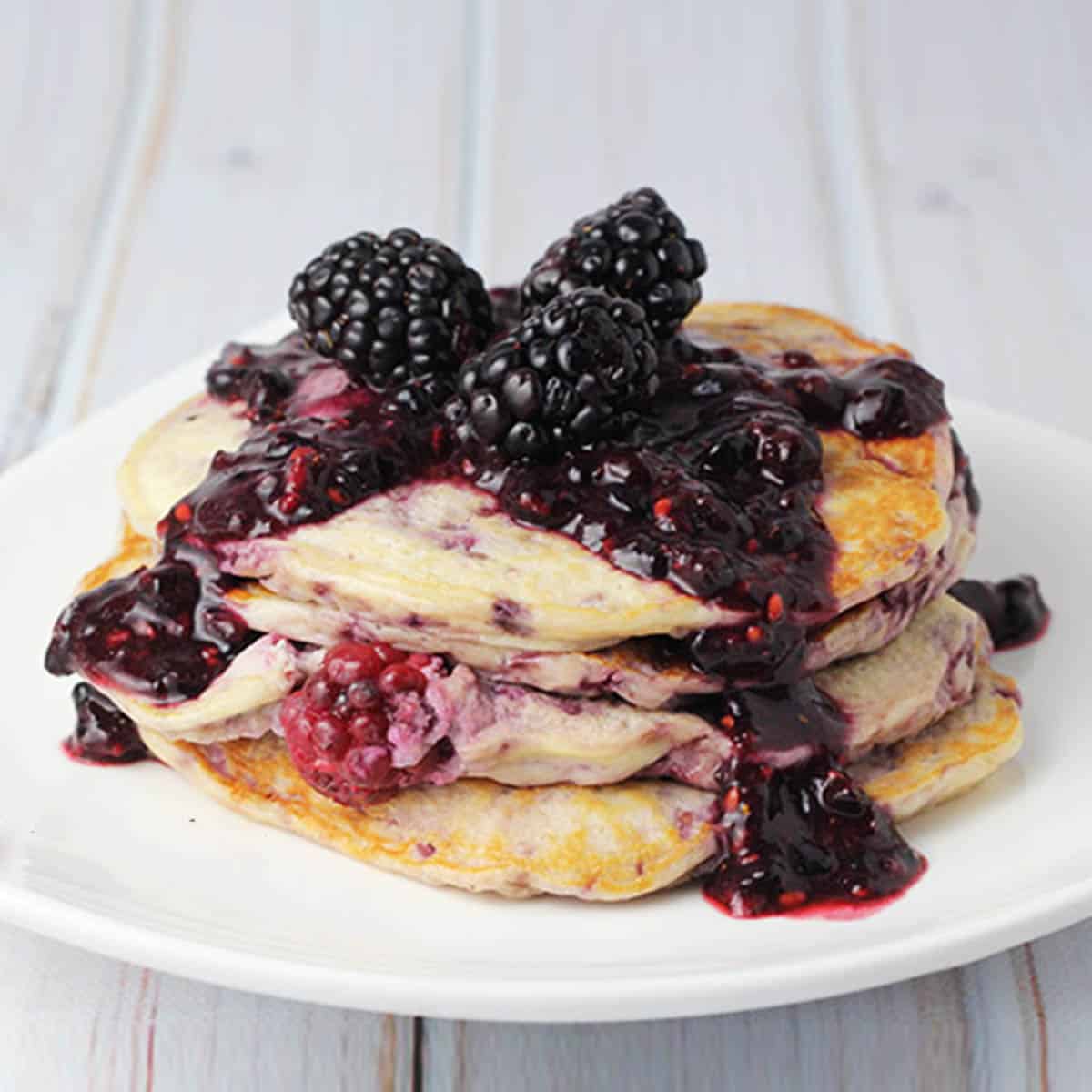 stack of ricotta pancakes topped with blackberry sauce and fresh blackberries