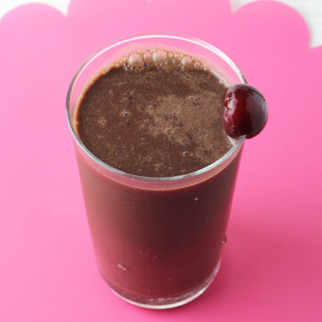 a glass with dark chocolate protein shake and a cherry on the rim of the glass