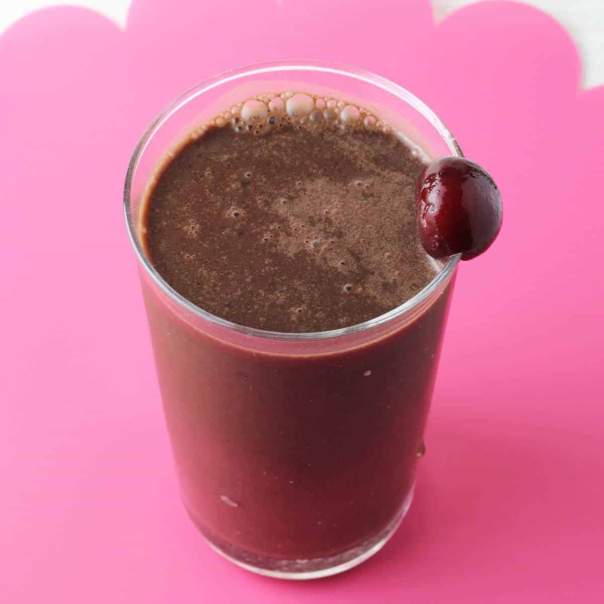 a glass with dark chocolate protein shake and a cherry on the rim of the glass