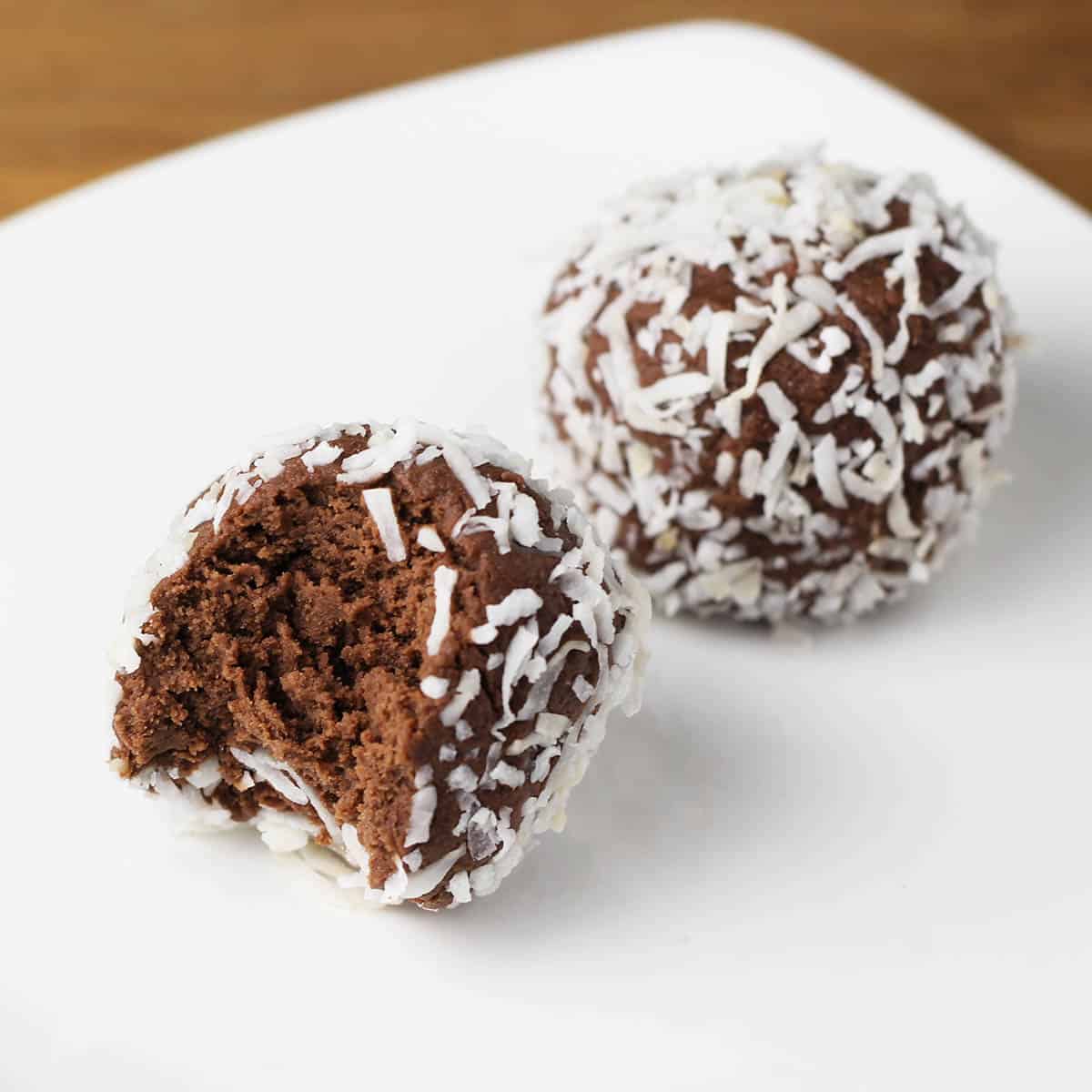 two chocolate protein cake balls covered in coconut shreds on a white plate