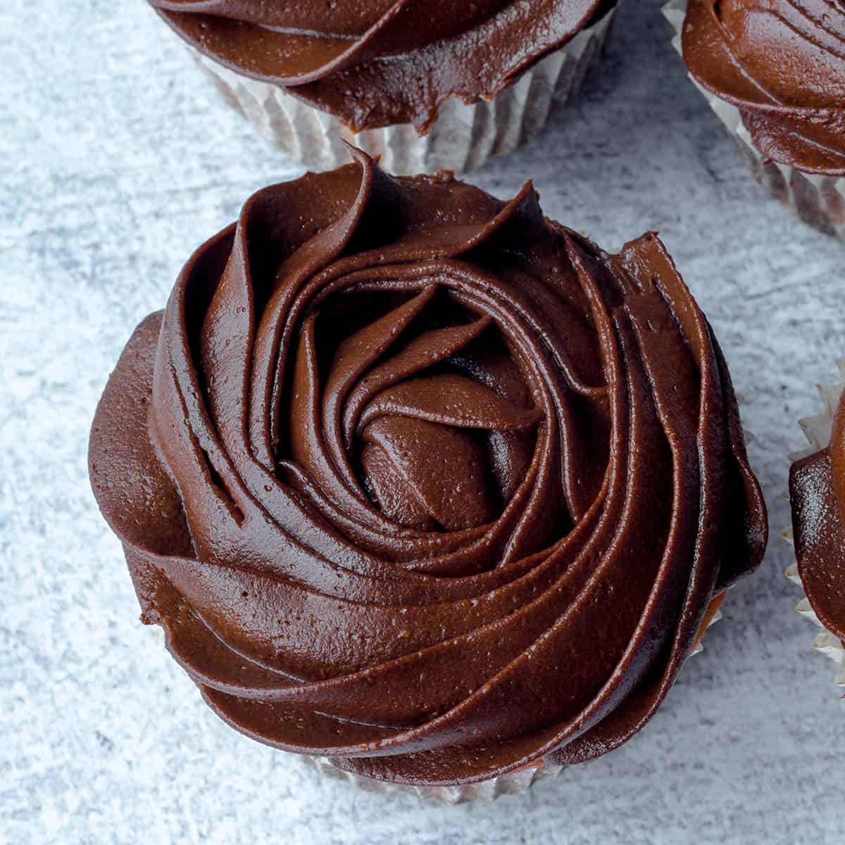 top view of smooth chocolate frosting in a rose shape on a cupcake with a grey background