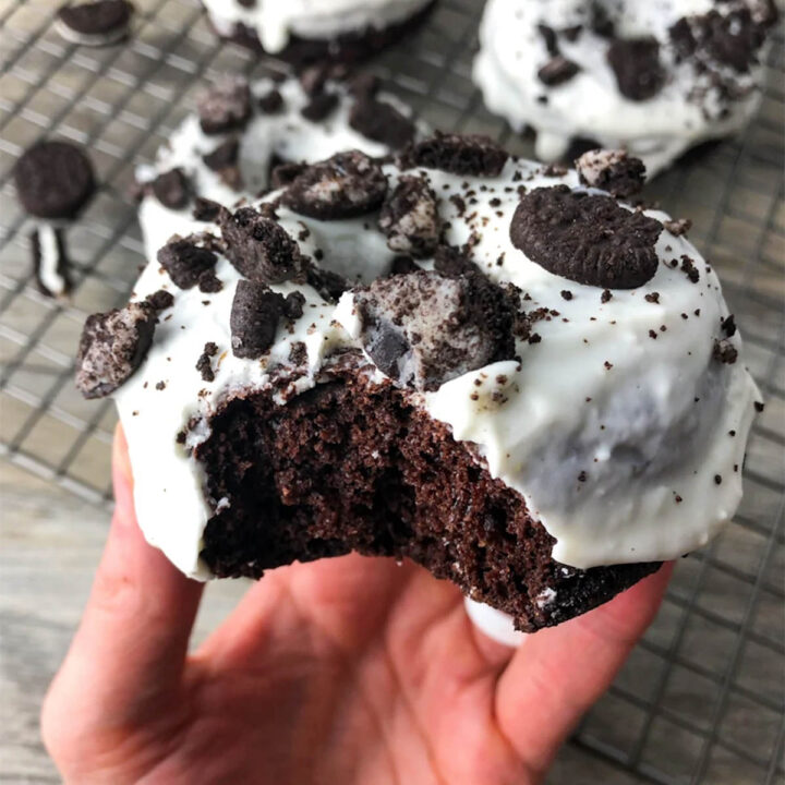 a bitten chocolate donut in a hand, topped with white icing and mini oreos