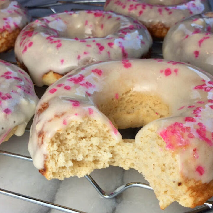 several iced donuts with pink sprinkles, one bitten in the front
