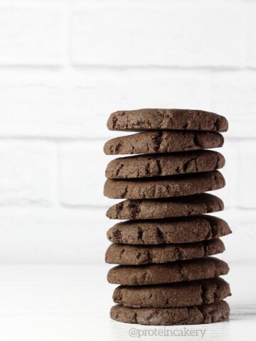 a stack of 10 chocolate cookies on a white table with a white brick background