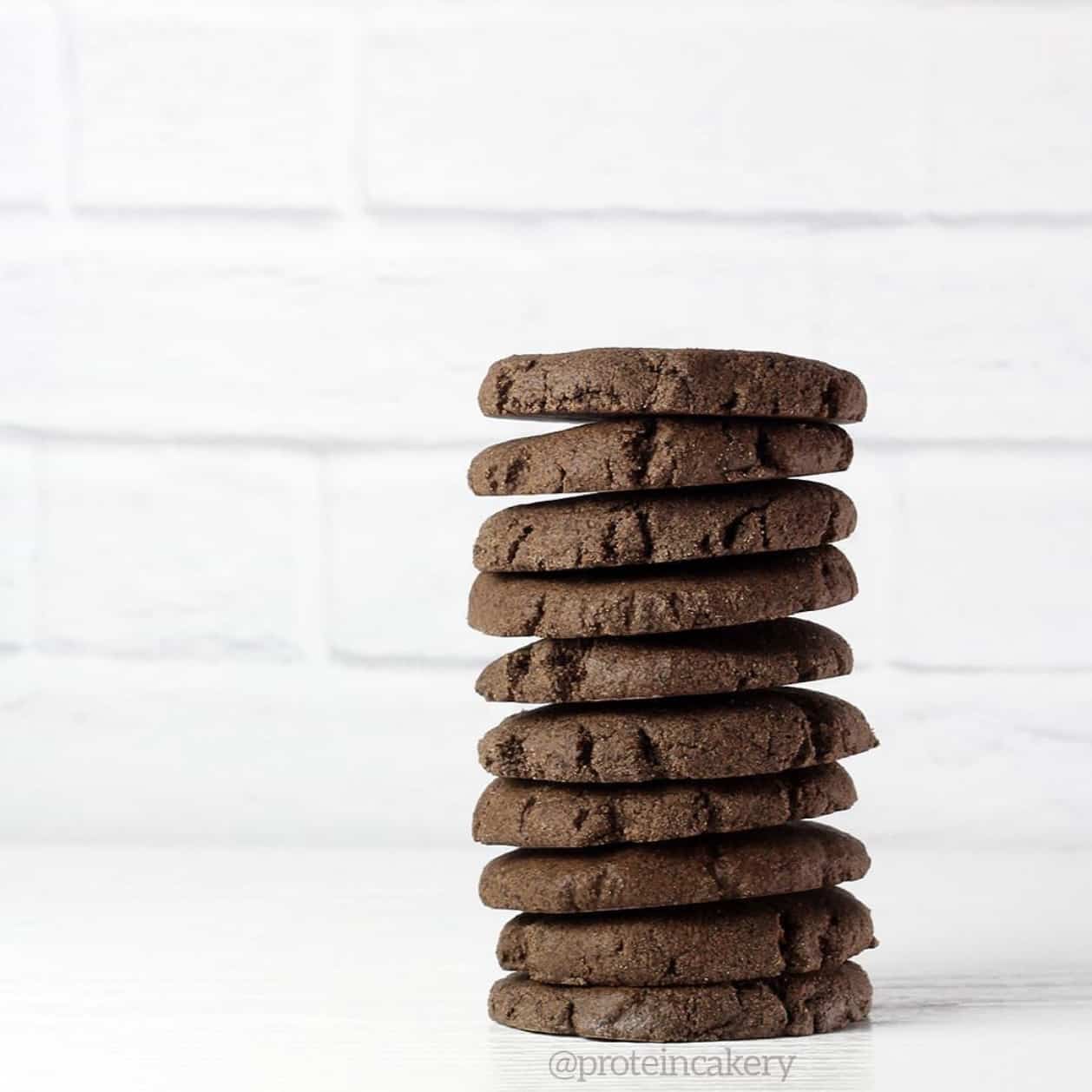 a stack of 10 chocolate cookies on a white table with a white brick background