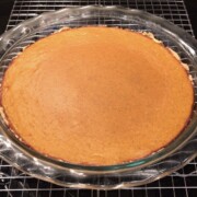 top view of pumpkin pie in a glass pie dish on a silver cooling rack