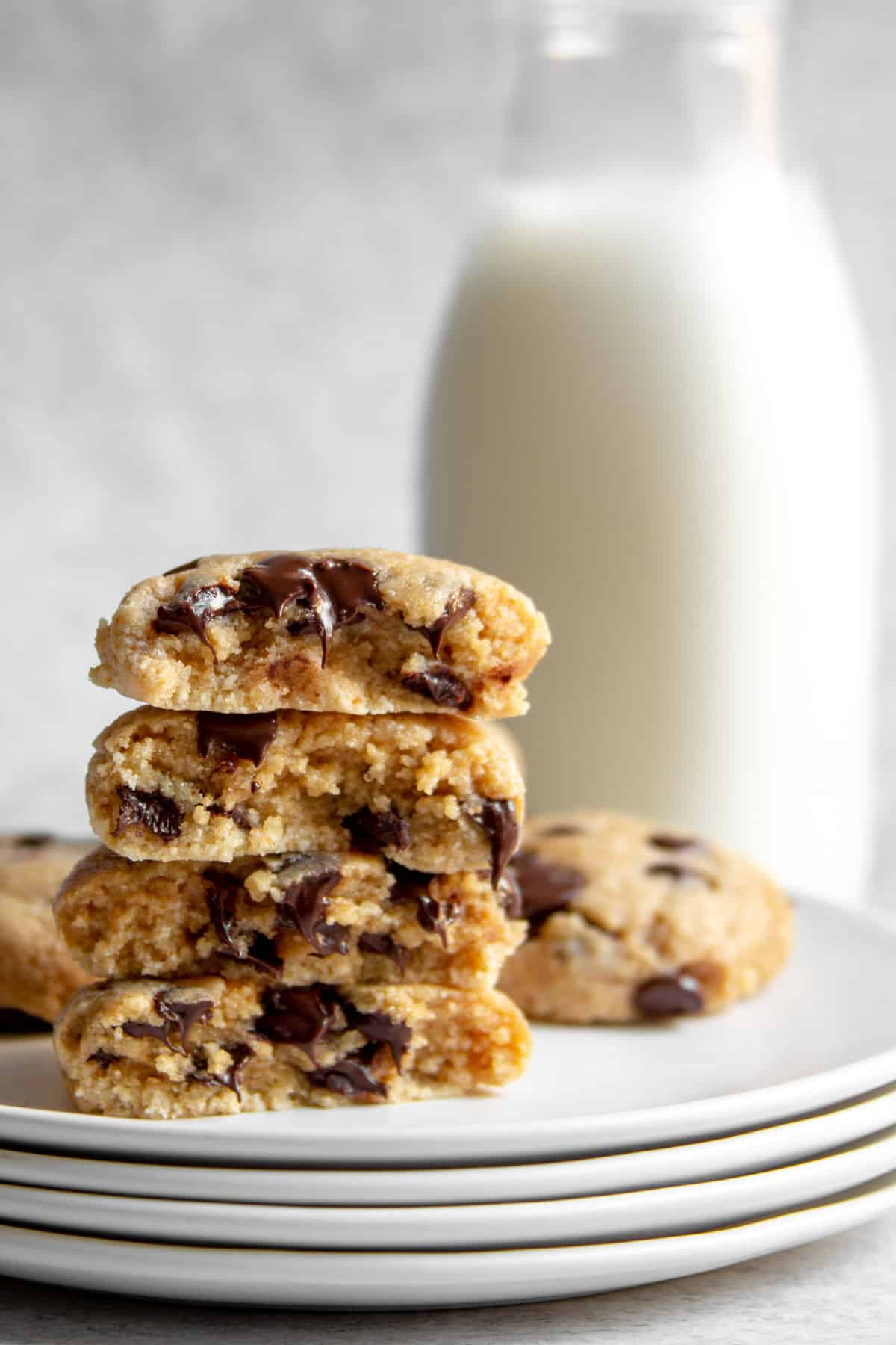 stack of four half cookies showing melted chocolate chips with milk in background