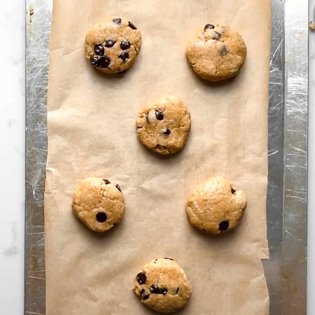 parchment lined cookie sheet with 6 unbaked chocolate chip protein cookies