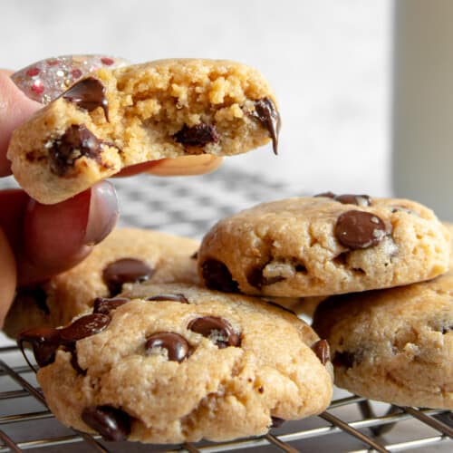 one bitten chocolate chip cookie being pulled from a pile of cookies