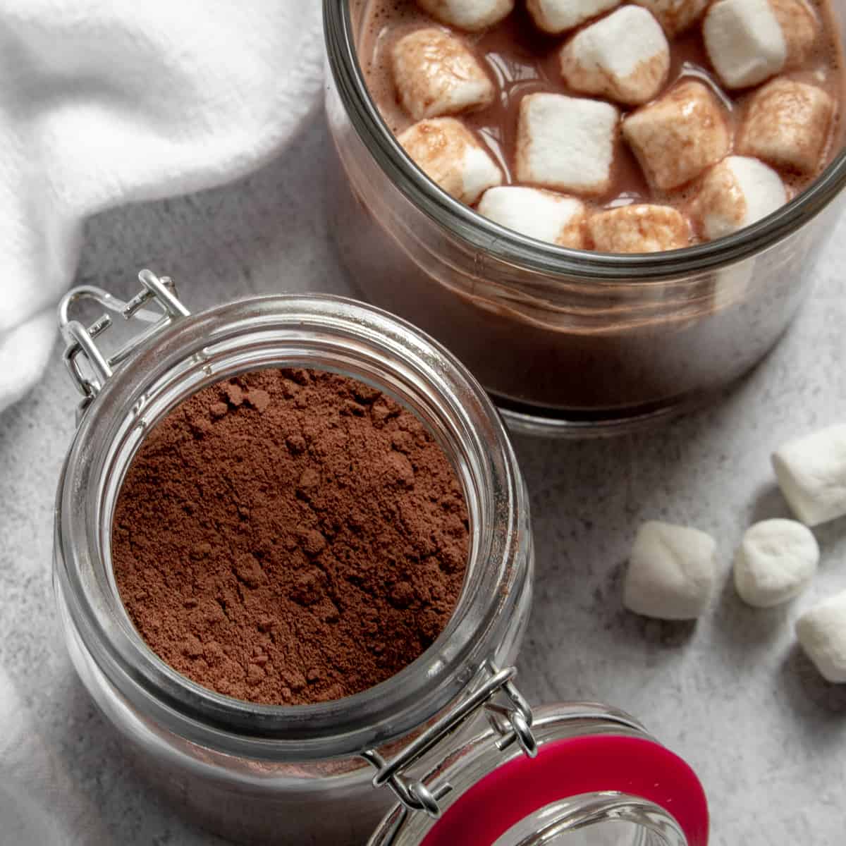top view of a jar of hot cocoa mix next to a mug of hot chocolate with mini marshmallows
