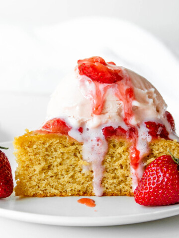 piece of vanilla protein cake topped with strawberry ice cream and fresh strawberries