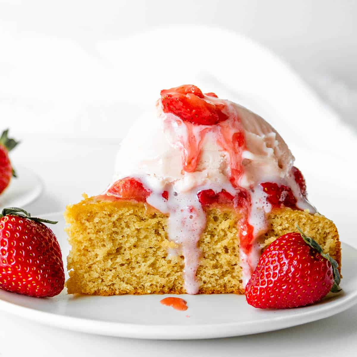 piece of vanilla protein cake topped with strawberry ice cream and fresh strawberries