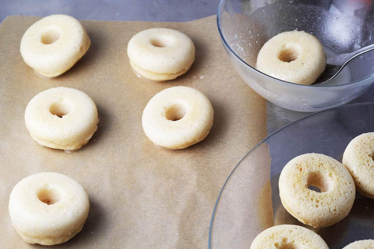 mini donuts being dipped in glaze and placed on parchment paper