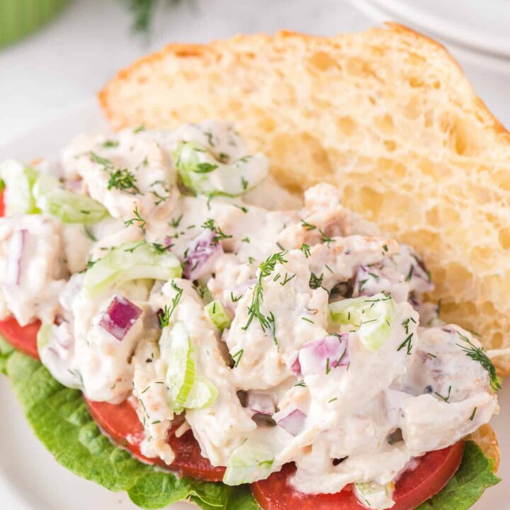 open chicken salad sandwich with lettuce, tomato, and dill.