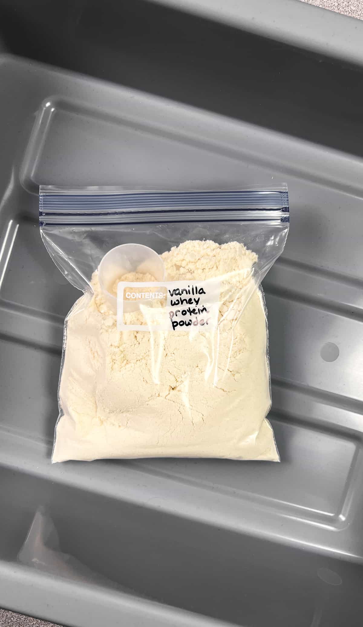 ziploc bag of vanilla protein powder in a grey TSA bin for airport security.