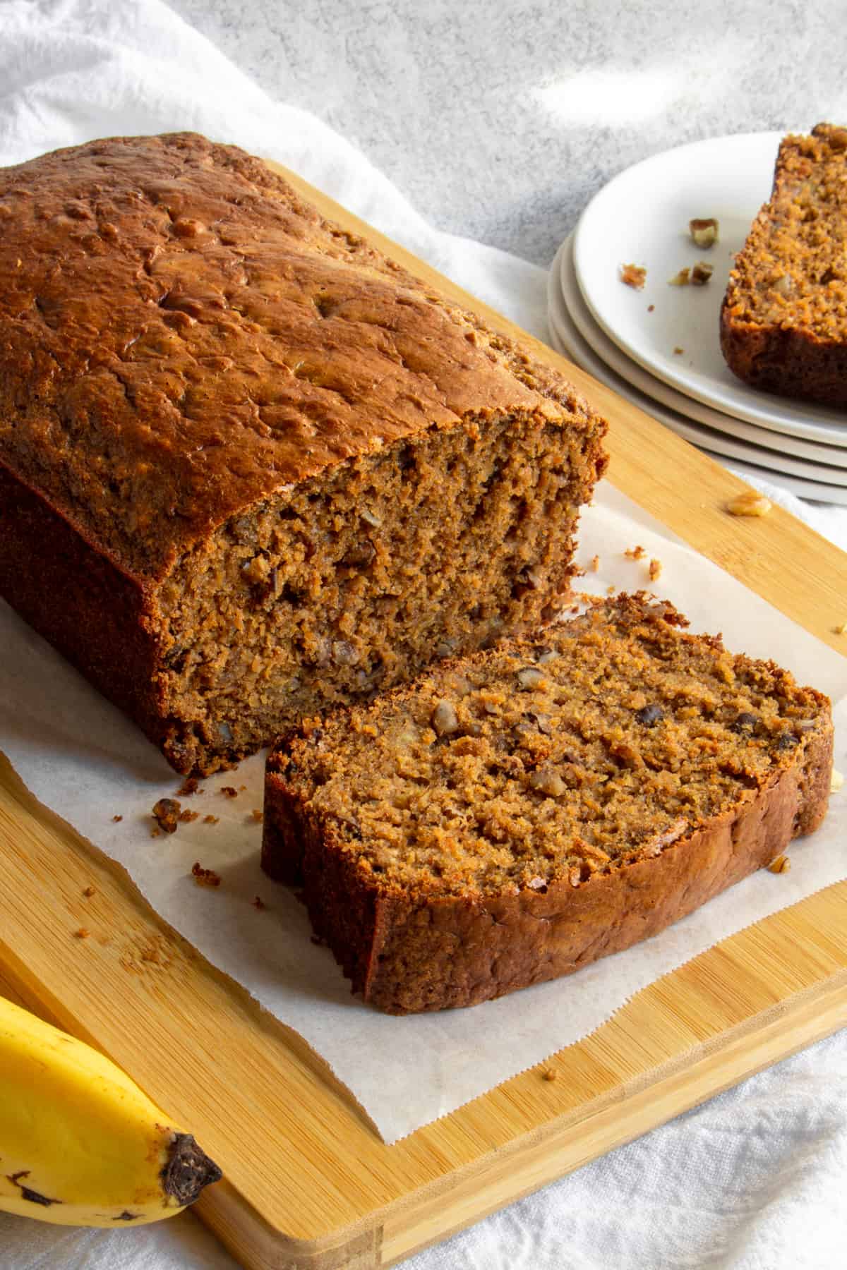 loaf of protein banana bread with a slice fallen in front, on a cutting board next to a banana.