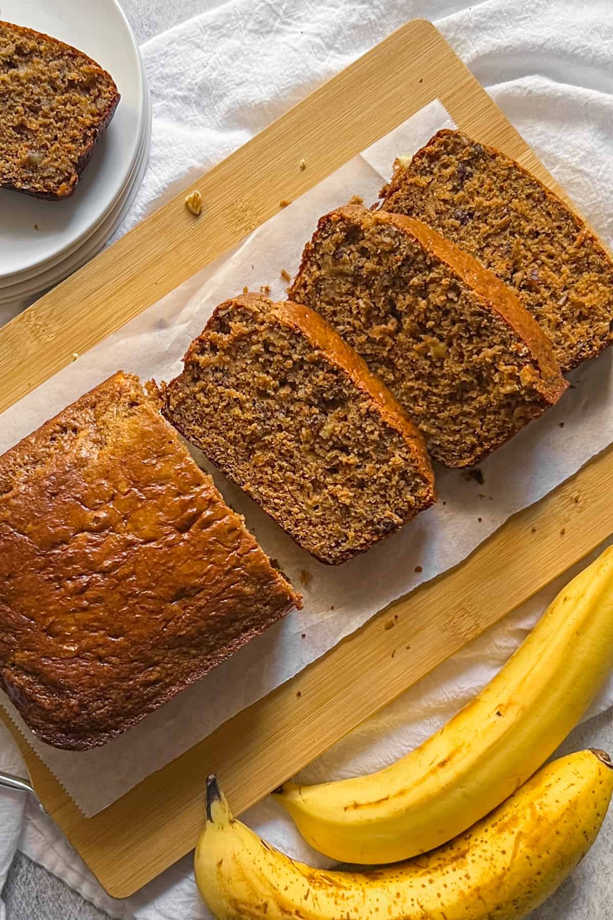 loaf of protein banana bread, partially sliced, on a cutting board with bananas in the front.