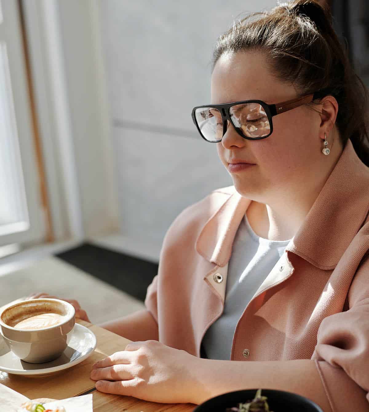 woman with down syndrome wearing glasses with a latte in front of her on a table.