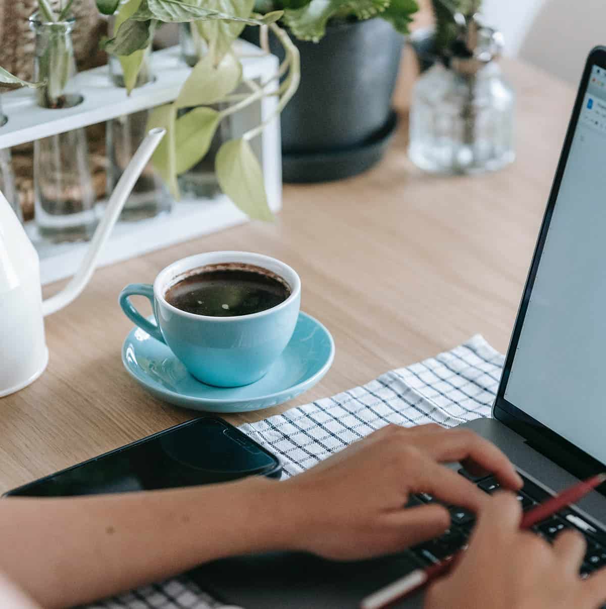 cup of black coffee in a turquoise mug next to a laptop.