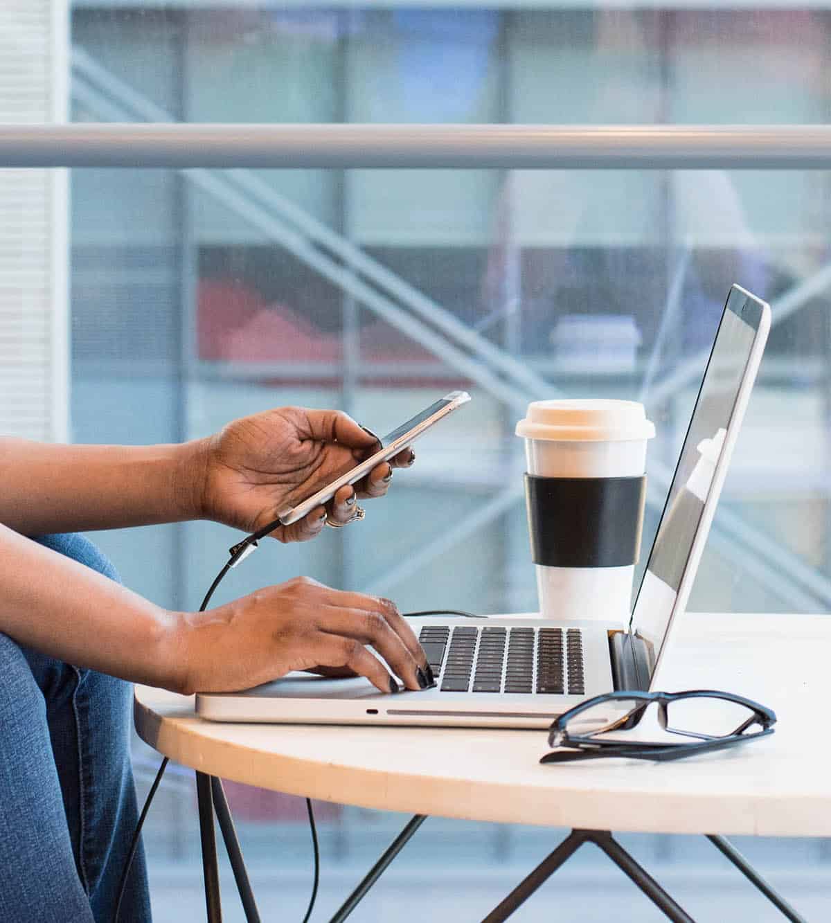 woman's hands with laptop, phone, coffee, and glasses.