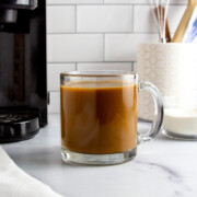 a glass mug with protein coffee next to a coffee maker