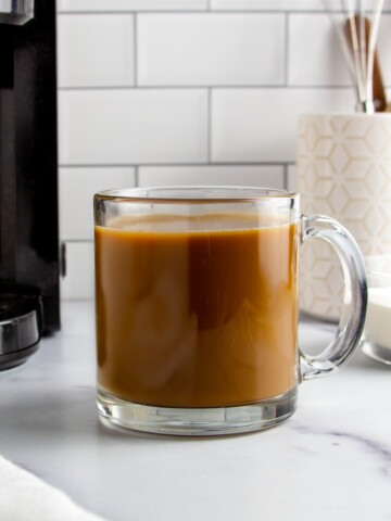 a glass mug with protein coffee next to a coffee maker