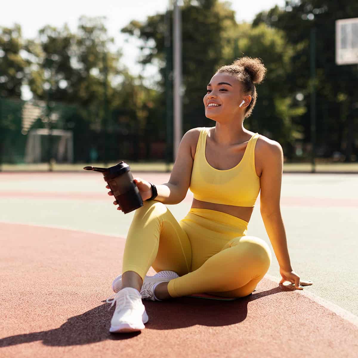 woman in yellow athletic gear holding a protein shake.