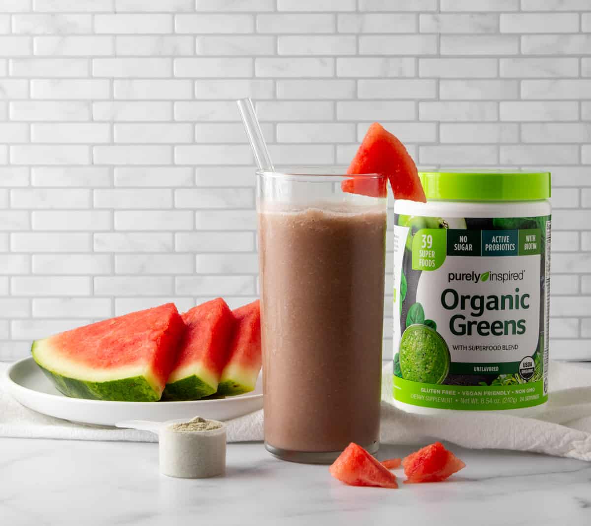 watermelon green drink next to a plate of watermelon slices and a container of green drink powder