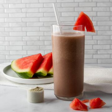 watermelon green drink next to a plate of watermelon slices and a scoop of green drink powder