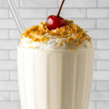 coconut protein shake in a milkshake glass with cream and a cherry on top.