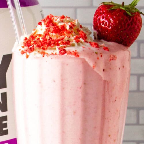 strawberry protein smoothie in a dessert glass in front of a tub of protein powder.