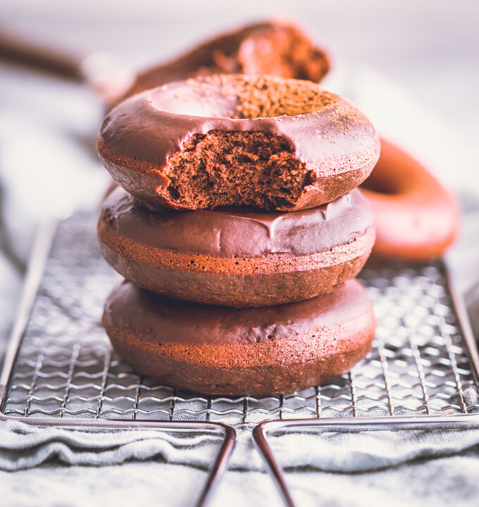 3 glazed chocolate donuts stacked on a cooling rack.