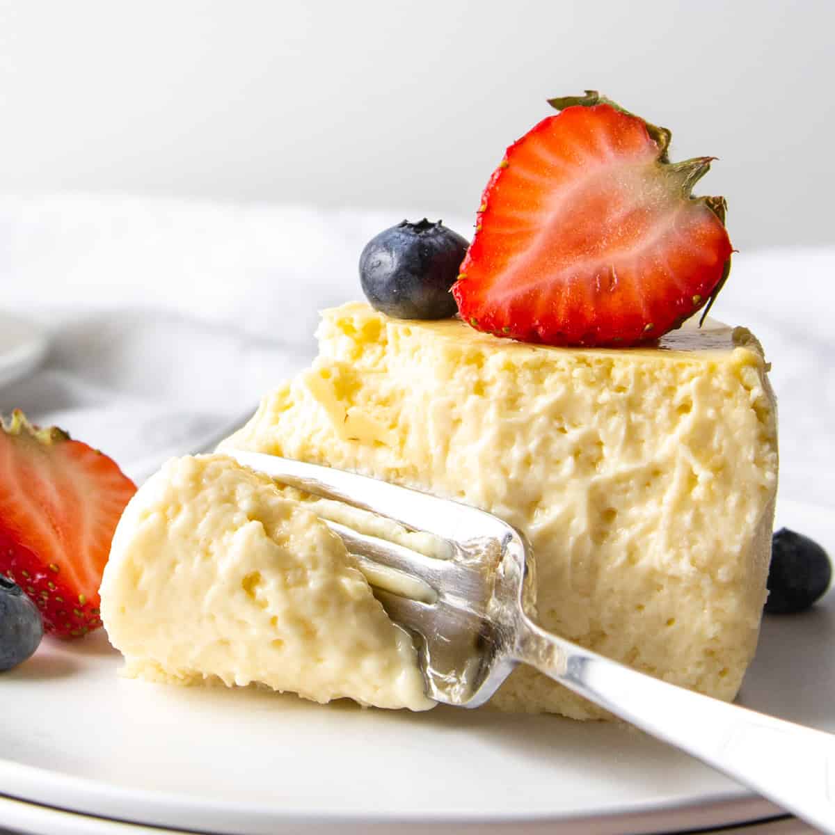 fork going through a piece of creamy protein cheesecake with berries.