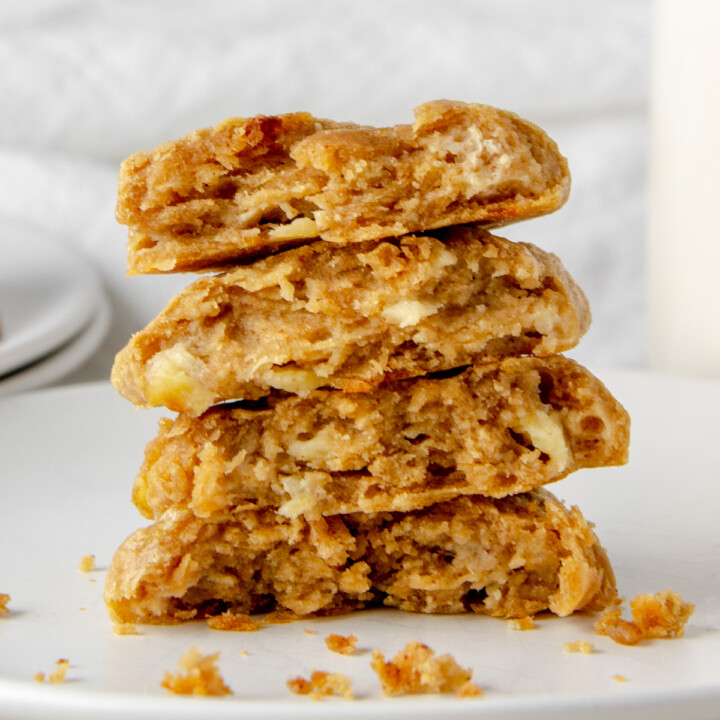 4 halves of banana peanut butter protein cookies stacked on a white plate with crumbs in front.