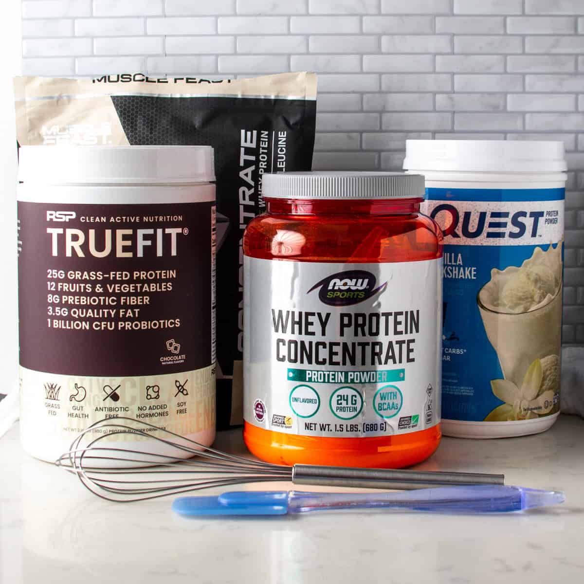 4 different protein powders with a whisk and spatula.