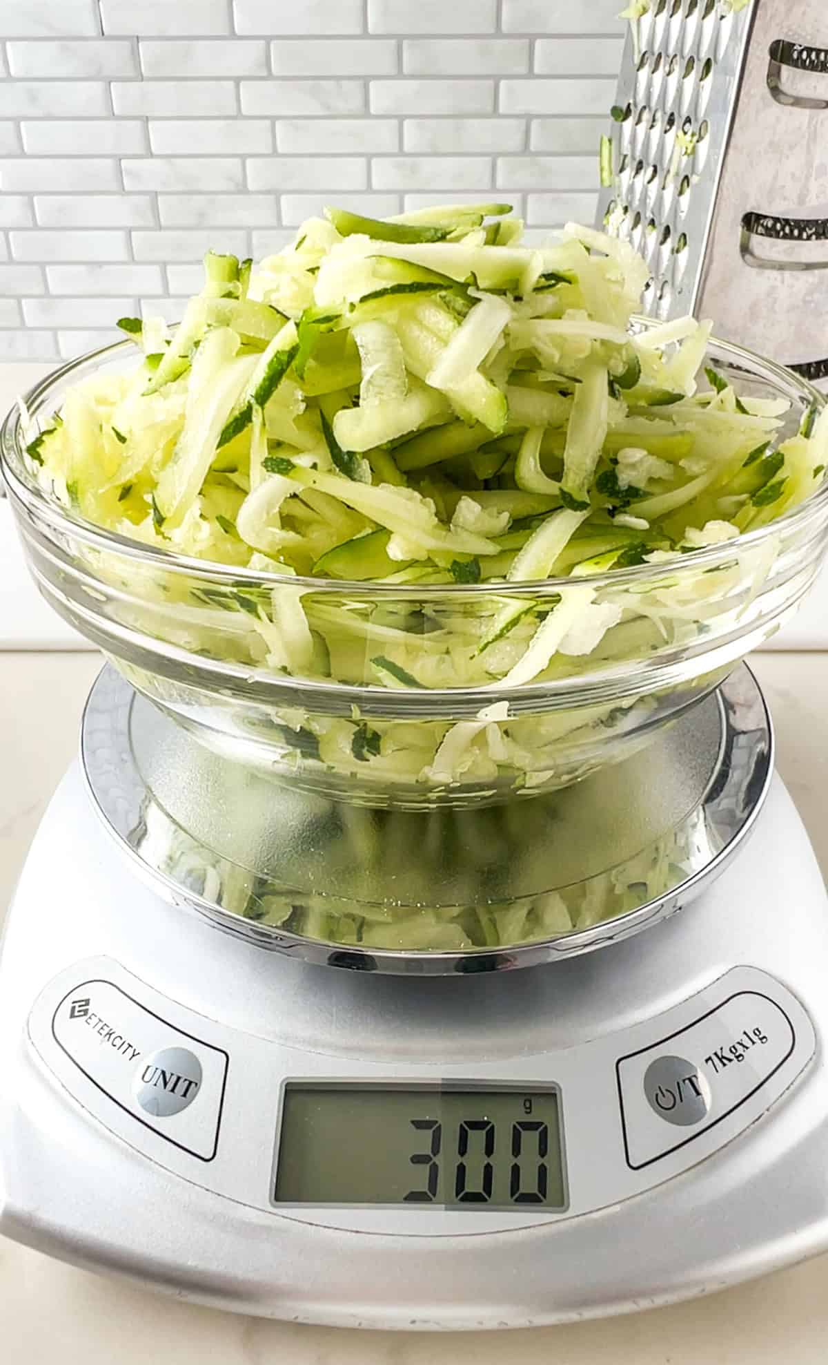 a bowl of shredded zucchini on a kitchen scale measuring 300g.