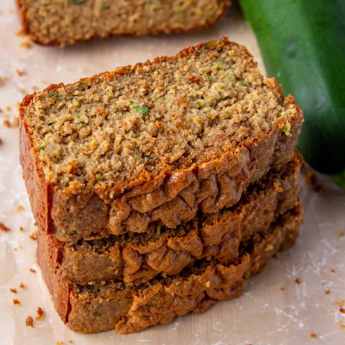 the stacked slices of high protein zucchini bread next to a zucchini.