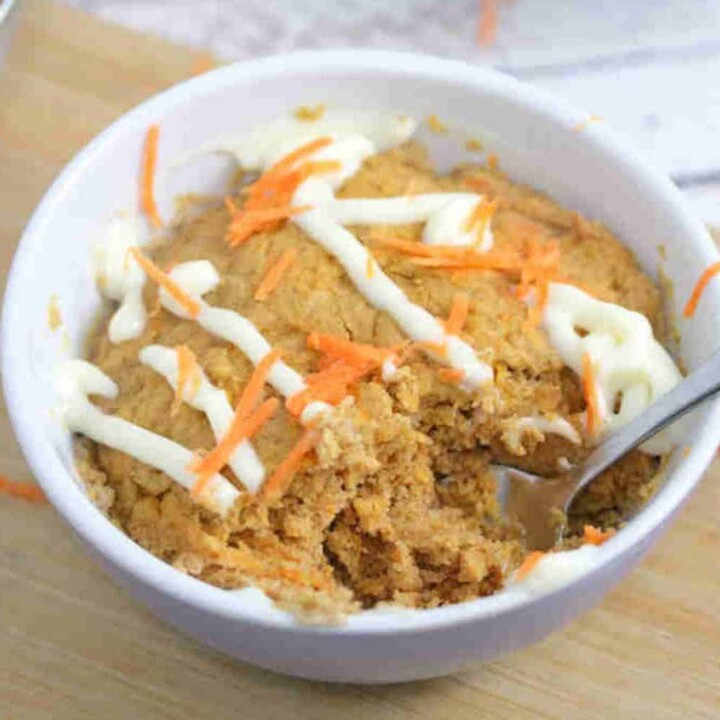 high protein carrot mug cake with drizzles of frosting and shredded carrots.