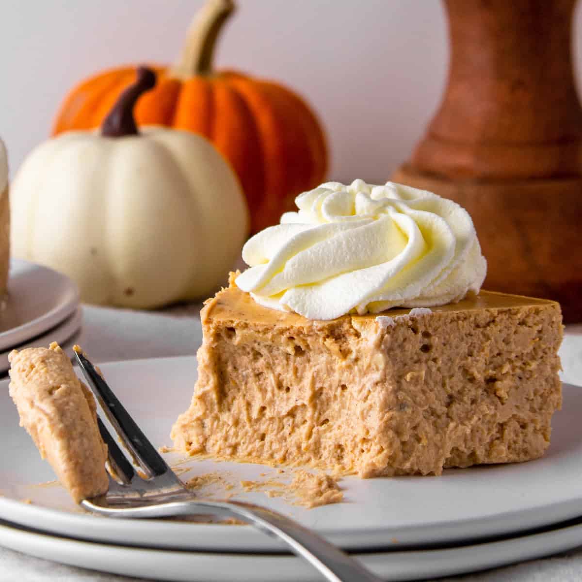 piece of pumpkin protein cheesecake topped with sugar free whipped cream, with a forkful of cheesecake.