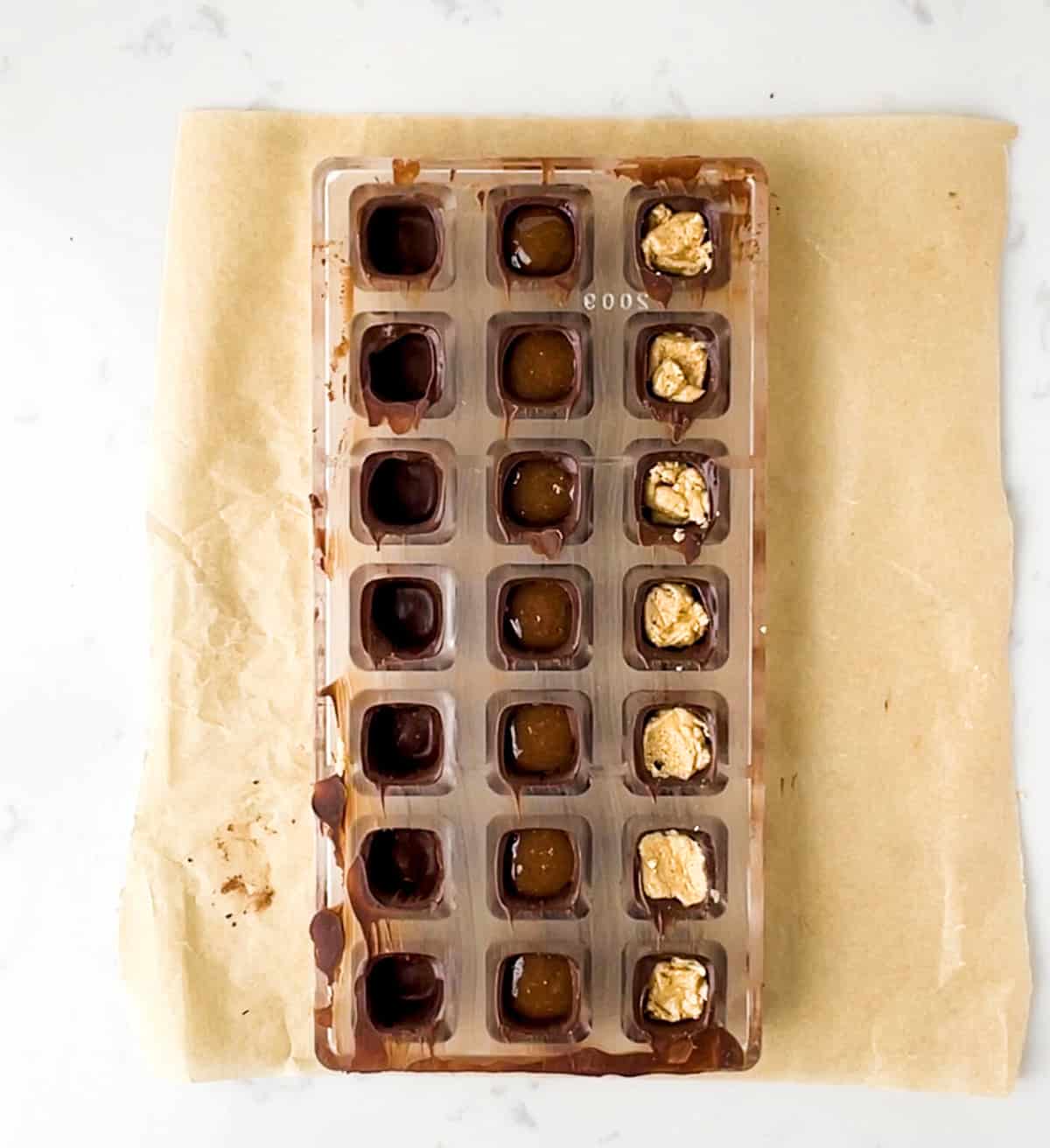 chocolate mold filled with outer chocolate shell and various fillings, ready to be topped off with chocolate.