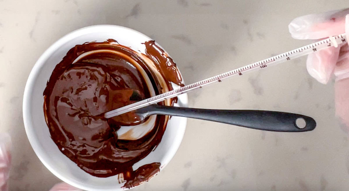 bowl of melted sugar free chocolate with a thermometer and a spatula.