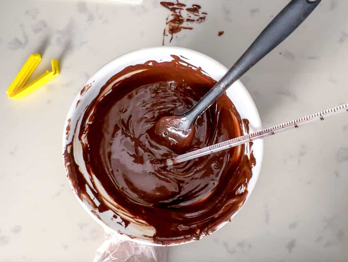 bowl of melted sugar free chocolate with a thermometer and a spatula.