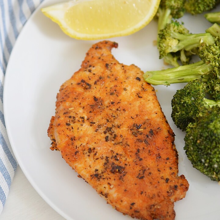 seasoned pork chop on a plate with broccoli and a wedge of lemon.