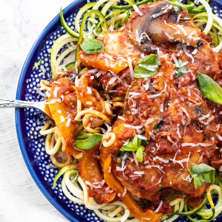 chicken cacciatore on a bed of zucchini noodles on a plate with a fork.