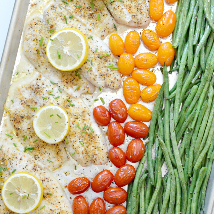 4 pieces of tilapia on a sheet pan with green beans and grape tomatoes.