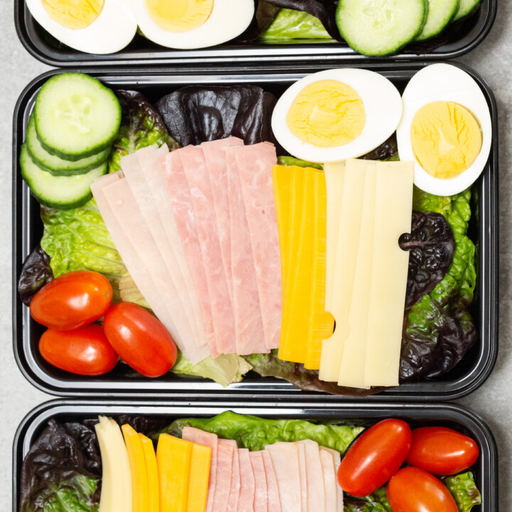 sliced meat and cheese with hard boiled egg on salad in a meal prep container.