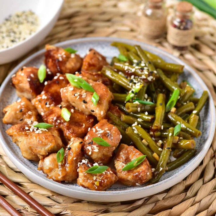 small pieces of chicken with cut green beans on a plate.