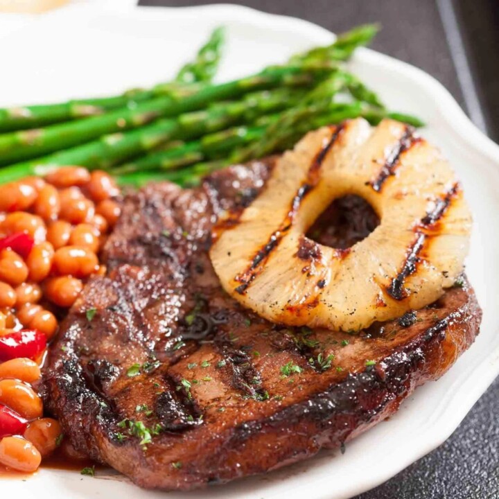 grilled pork chops topped with a slice of pineapple next to bean salad.