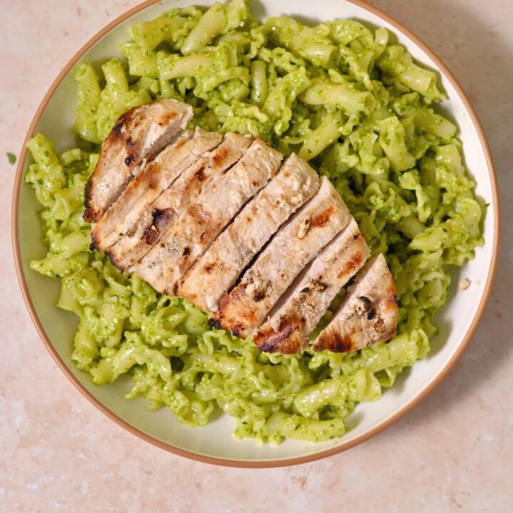 a plate of protein pesto pasta with sliced chicken.